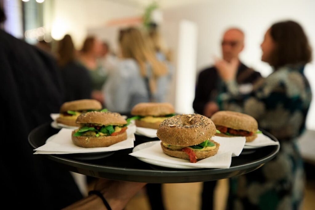 A close-up shot of canapés on white napkins on a black tray, with attendees chatting in the background.