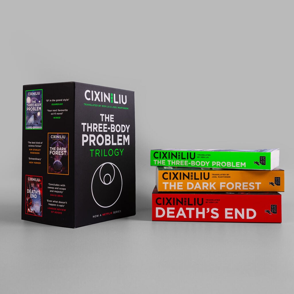 A photograph of the trilogy and boxset for The Three-Body Problem. The black boxset packaging stands to the left, with the trilogy of paperbacks stacked on top of each other to the right.