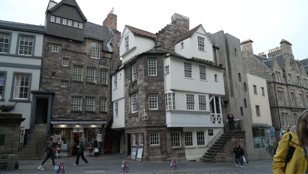 Exterior view of historic stone and timber-framed medieval buildings along The Royal Mile in Edinburgh, including the Scottish Storytelling Centre, with pedestrians walking along the pavement on an overcast day.