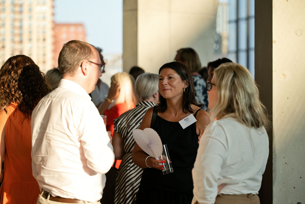 A group of three Maykn launch attendees speaking on the balcony after the panel, with golden light hitting the wall behind them.